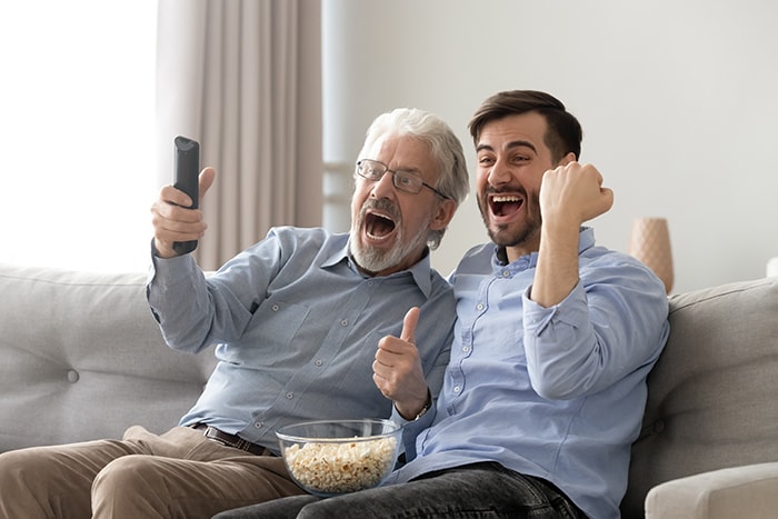 Father and son with a bowl of popcorn cheering at a tv